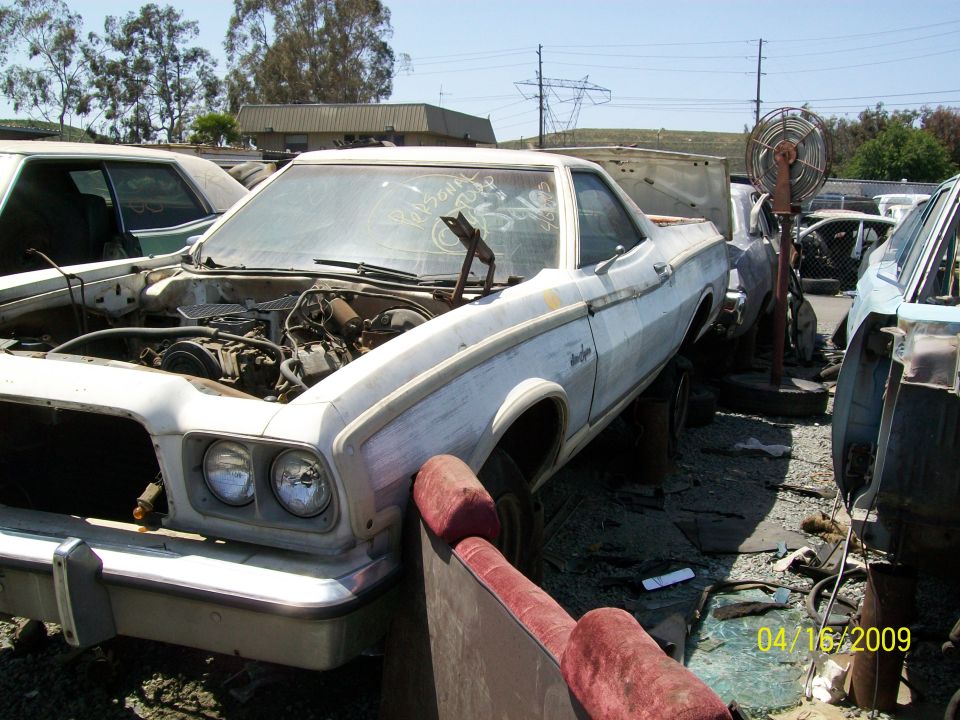 White 1972 Ford Ranchero with hood open, showing engine, in a junkyard