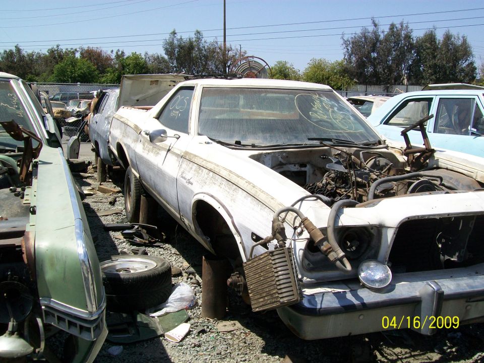 White 1972 Ford Ranchero with open hood and missing parts in a junkyard