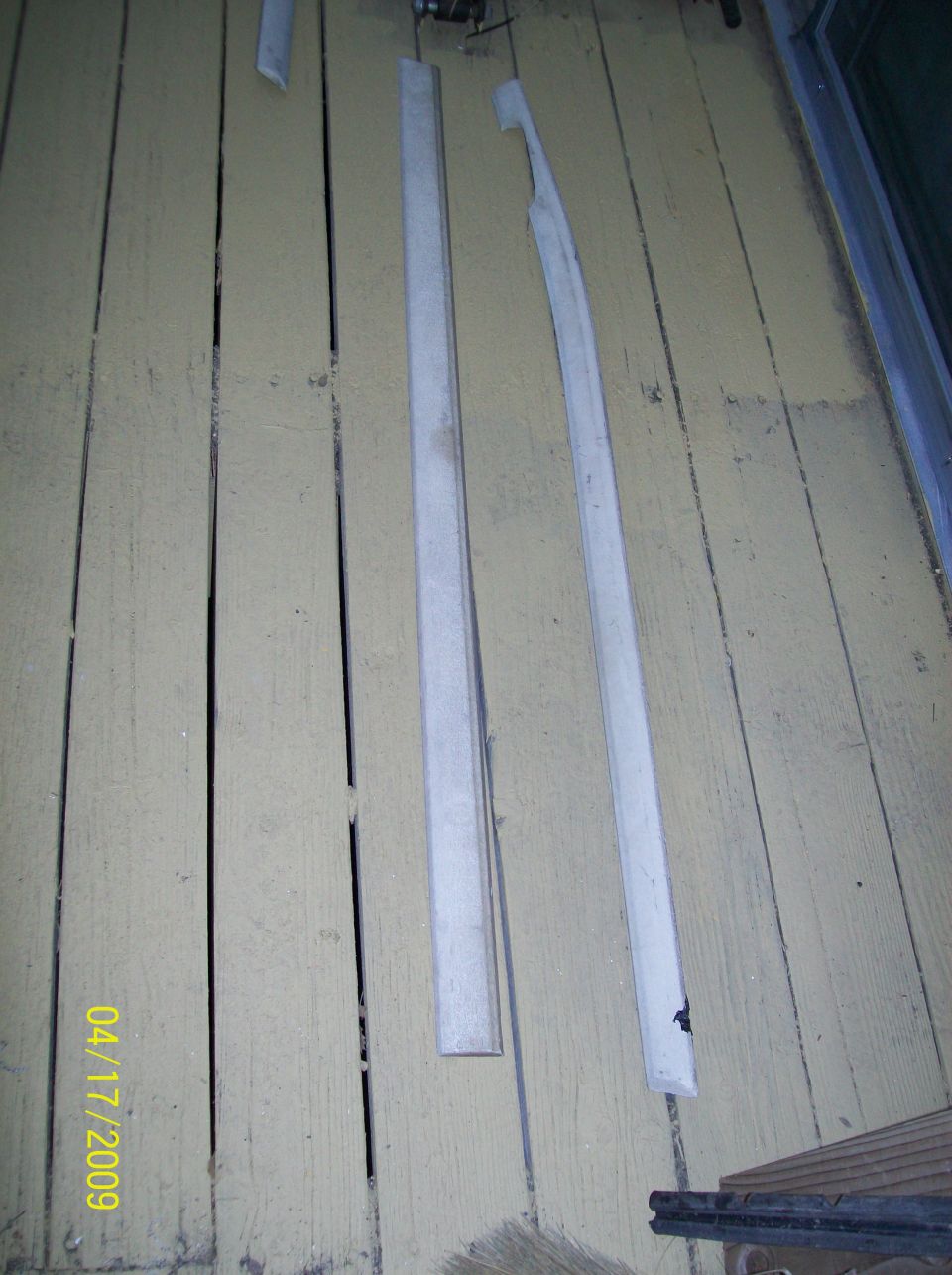 Three metal trim pieces laid out on a weathered wooden floor. Date stamp '04/17/2009' visible