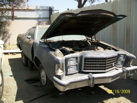 1972 Ford Ranchero - A weathered 1977 Ford Ranchero sits in a junkyard with its hood propped open, revealing the engine bay.