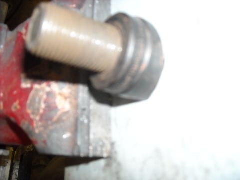 1979 Ford F-150 - A threaded bolt is secured in a red clamp, with focus on the bolt's threads and the clamp's jaws.