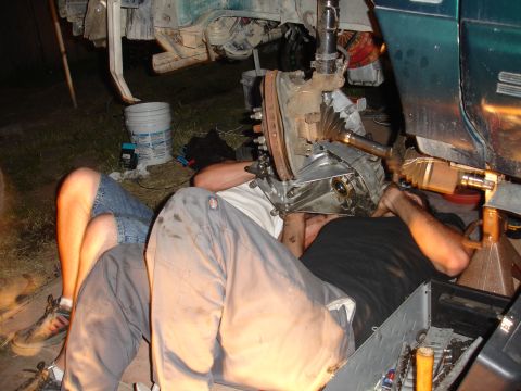 1995 Ford Taurus - Two mechanics are working underneath a vehicle, focused on the transmission and drive axle assembly.