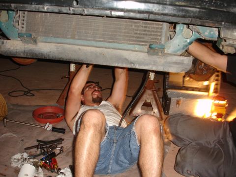 1995 Ford Taurus - A person works on the underside of a vehicle supported by jack stands, with tools and a drain pan nearby.