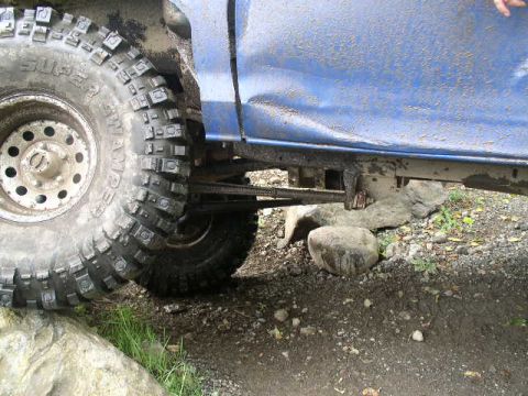 1979 Ford Bronco - The side view of a blue vehicle shows its large off-road tire and suspension system, with rocks on the ground.