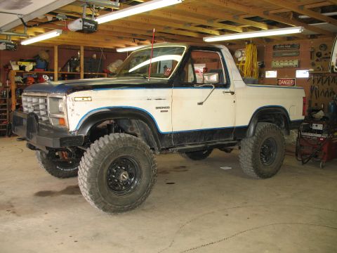 1985 Ford Bronco - A two-tone Ford Bronco sits in a garage, modified with off-road tires.