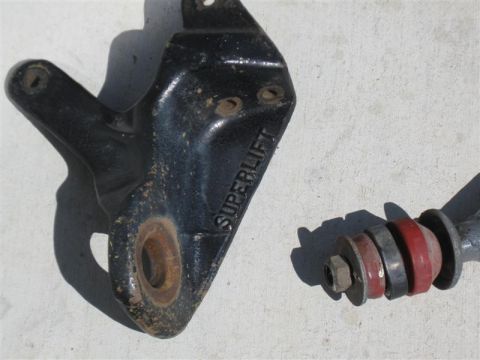 1986 Ford Bronco - A black bracket labeled 'SUPERLIFT' is shown next to a suspension component with red bushings, likely part of a vehicle lift kit.