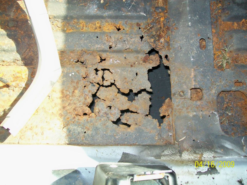 Rusted floor pan with large holes and corrosion