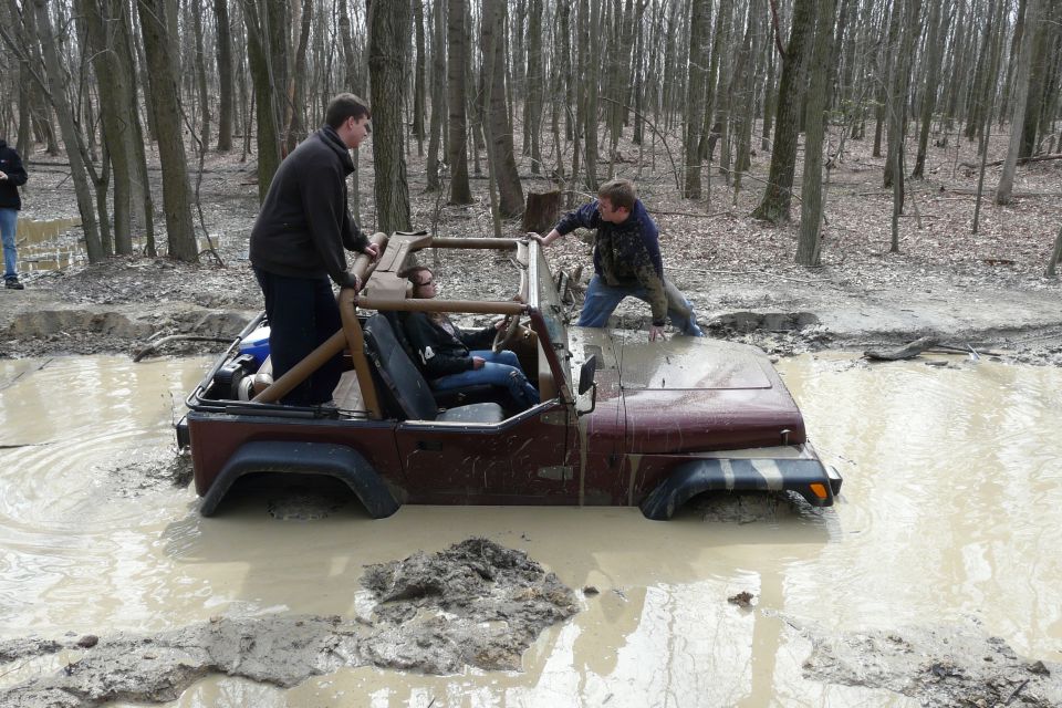 Jeep stuck in mud pit with people trying to push it out