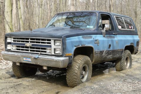 1995 Ford Bronco - This Chevrolet K5 Blazer, likely from the 1980s, is stuck deep in mud on a wooded trail.