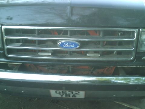 1989 Ford Bronco - Close-up of a Ford truck's front grille, the iconic blue oval emblem and a license plate.