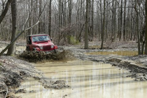 1995 Ford Bronco - Jeep Wrangler navigating a muddy obstacle in a wooded area.
