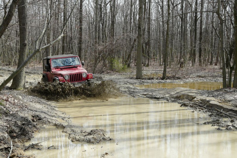 Red Jeep Wrangler splashing through a muddy trail in a forest