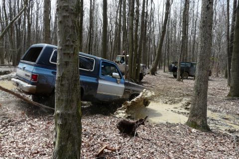 1995 Ford Bronco - Multiple SUVs navigate a muddy trail through a dense forest.