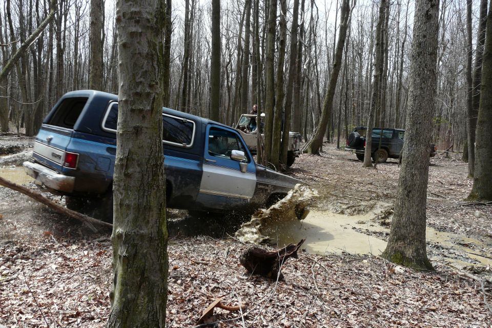 Blue and silver SUV stuck in mud, trees and other vehicles in background