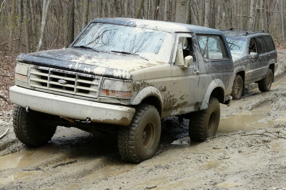 1995 Ford Bronco driving through mud with a Jeep Grand Cherokee behind it