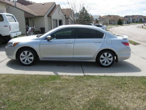 2009 Honda Accord - A silver sedan is parked on a driveway in front of a residential house, showing its side profile.