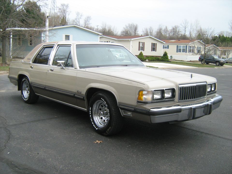 Tan 1988 Mercury Grand Marquis parked in front of houses. Chrome wheels and a vinyl top