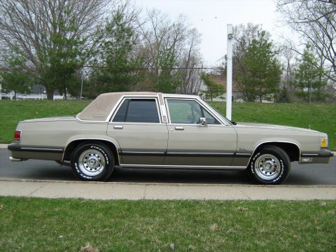 1988 Mercury Grand Marquis - A 1988 Mercury Grand Marquis sedan is shown from the side, parked on a street with a vinyl roof and chrome wheels.
