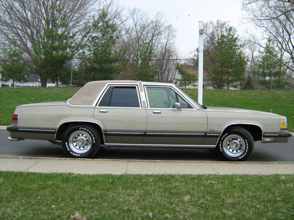 Tan 1988 Mercury Grand Marquis sedan, side view, chrome wheels, vinyl roof, on a paved surface with grass