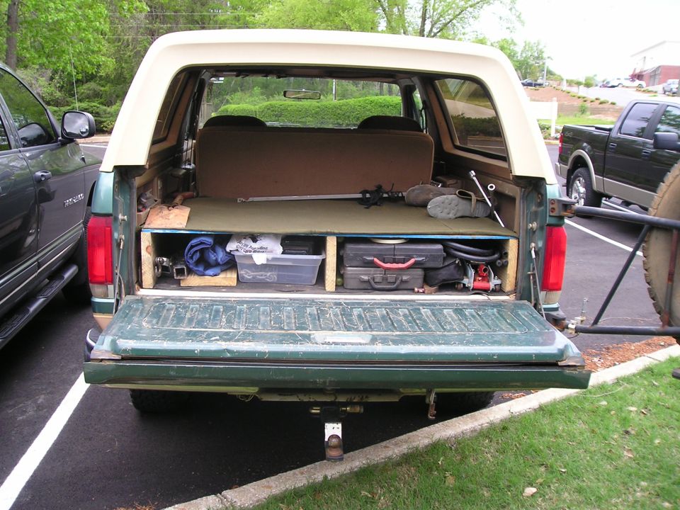 Rear of a green Ford Bronco with tailgate down showing plywood cargo deck and tool storage