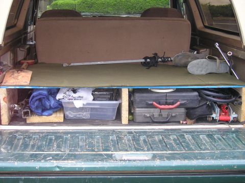 1989 Ford Bronco - The rear storage area of a vehicle is organized with various items, including tools and a decorative sword.