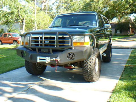 1992 Ford Bronco - A dark green 1992 Ford Bronco is parked on a concrete driveway, modified with a heavy-duty bumper and winch.