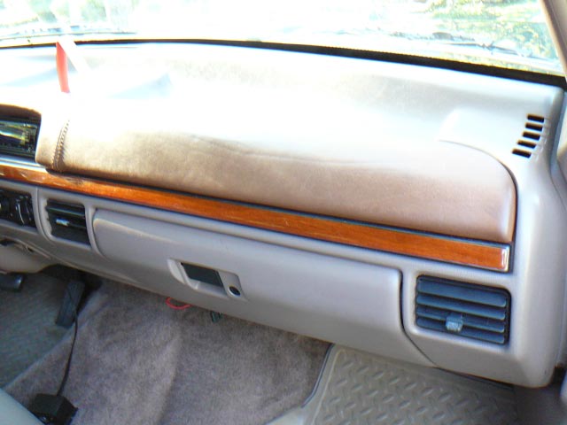 Dashboard of a vehicle with wood trim and tan upholstery. Glove box and air vents are visible