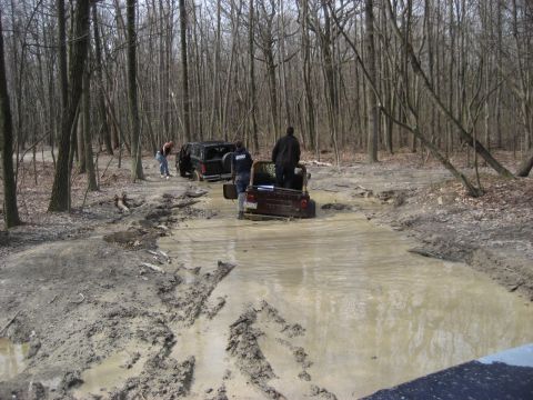 1991 Ford Bronco - Two SUVs are stuck in a muddy forest road, with people around them.