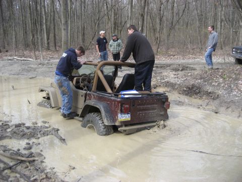 1991 Ford Bronco - People gather around a Jeep Wrangler stuck in a muddy off-road trail.