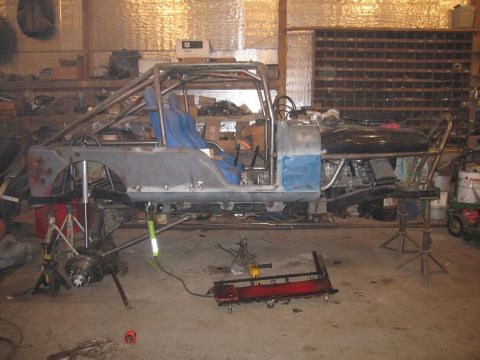 1992 Ford Bronco - A custom vehicle build is underway in a workshop, a roll cage and exposed suspension components.