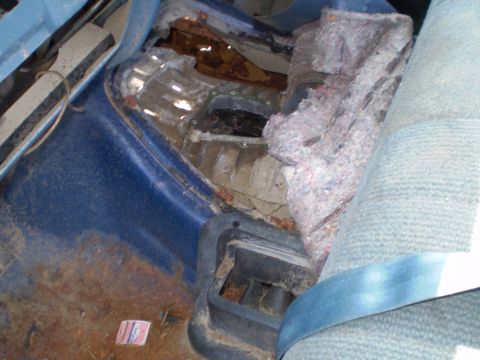 1995 Ford F-150 - The rear passenger side floor of a 1995 Ford F-150 shows significant rust damage and torn interior upholstery.