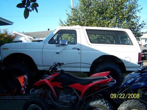 1982 Ford Bronco - A white 1980s Ford Bronco is parked next to two ATVs on a sunny day.