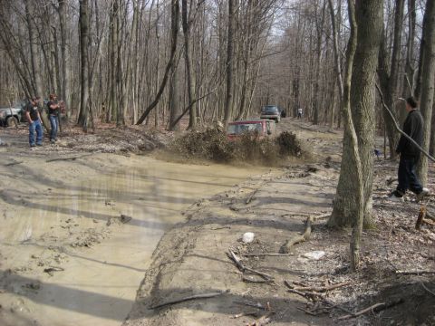 1991 Ford Bronco - Off-roading in the woods, with multiple vehicles tackling a challenging muddy trail.