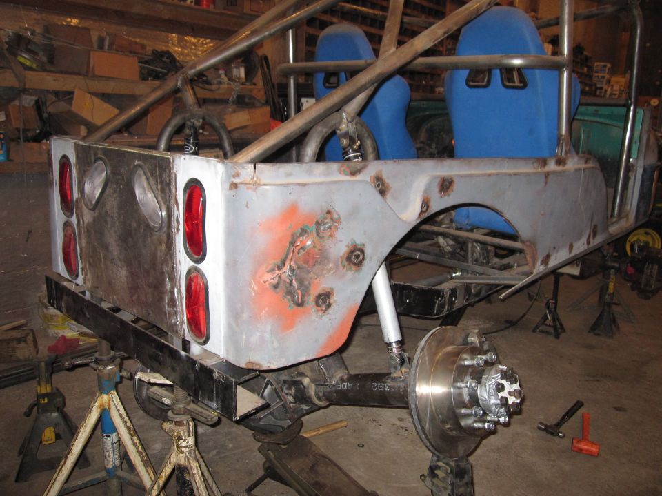 custom off-road vehicle body with roll cage and blue racing seats, being worked on in a garage