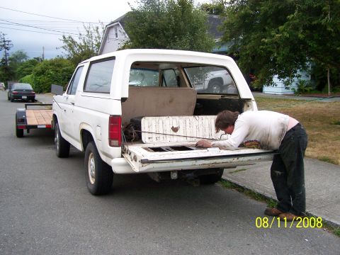 1982 Ford Bronco - A white Ford Bronco from the 1980s is seen from the rear, towing a trailer, with a person attending to the tailgate.