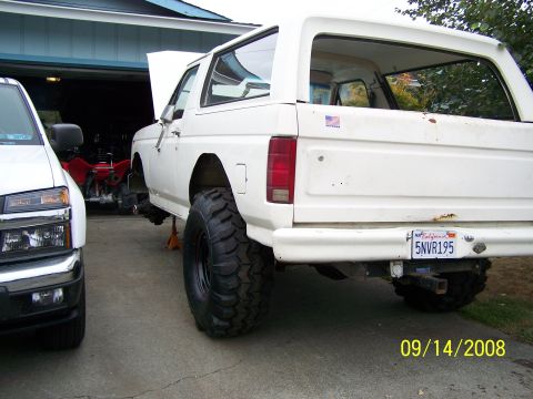 1982 Ford Bronco - A white SUV is parked in a garage with its hood open and lifted on jack stands, next to a white pickup truck.