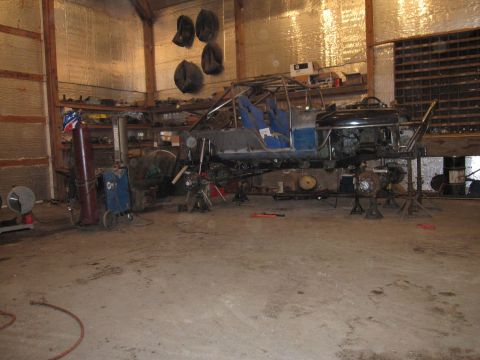 1992 Ford Bronco - Custom buggy frame with roll cage and blue seats, raised on jack stands in a workshop.