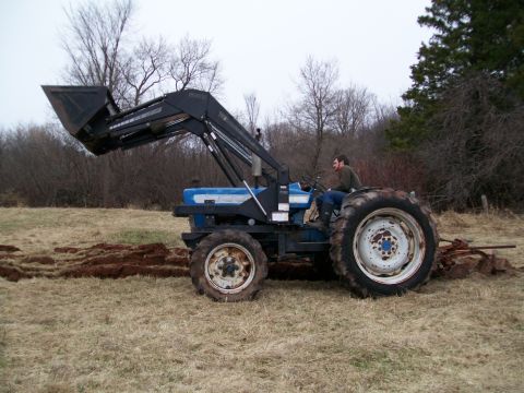 2000 Chevrolet Tahoe - A blue tractor with a front loader is seen from the side, operating in a field.