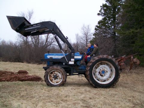 2000 Chevrolet Tahoe - Tractor with front loader carrying two people in a field with trees in the background.
