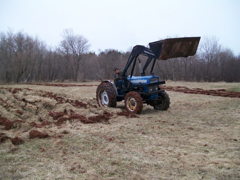 Blue tractor with front loader plowing a field