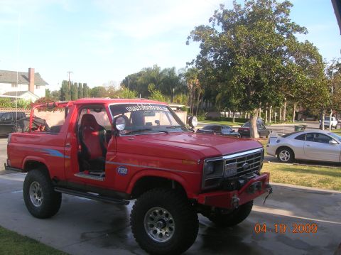 1985 Ford Bronco - This heavily modified red Ford Bronco has racing seats and large off-road tires. A silver car is parked behind it.