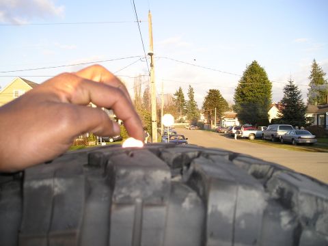 1997 Ford F-250 - A finger points to a small white object on a tire tread, with a street and houses in the background.