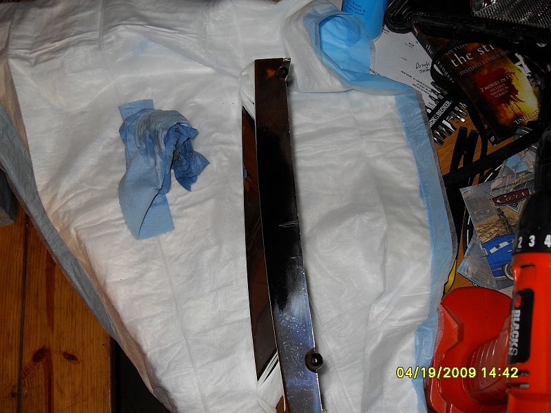 Shiny car trim piece on absorbent pads with a blue rag and a drill in the background