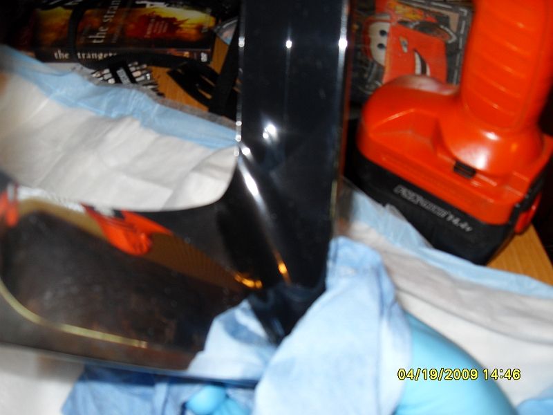 Black car fender with chrome trim being wiped with a blue cloth, orange power tool in background