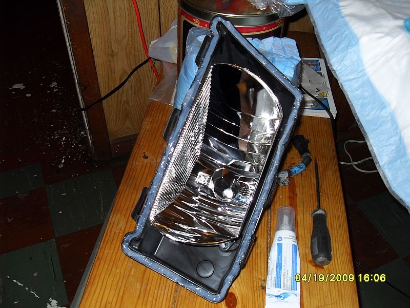 Headlight assembly with sealant applied, next to a tube of sealant and a screwdriver