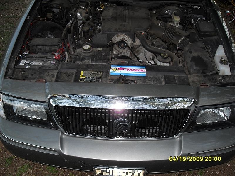 Silver sedan's engine bay and front grille. The grille has vertical bars and a Mercury emblem. A Thrust amplifier is visible