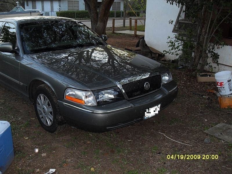Gray Mercury Grand Marquis parked outside a house. Front end visible