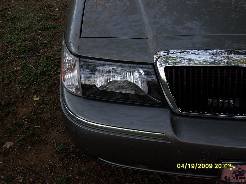 Front corner of a gray 2004 Mercury Grand Marquis showing headlight and chrome grille