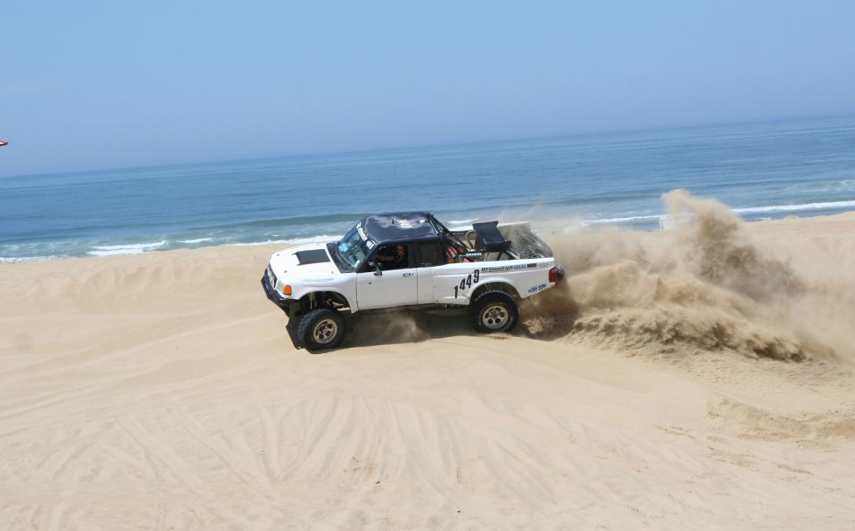 White pickup truck with roll cage kicking up sand on a beach