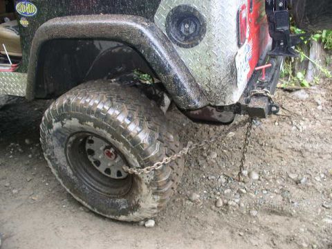 1979 Ford Bronco - A close-up view of a muddy Jeep Wrangler's rear tire and fender, with a chain secured to its bumper.